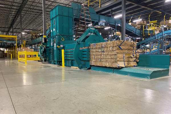 blue baler in a large warehouse with conveyors feeding the large blue hopper