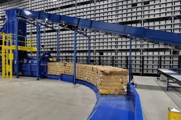 Blue conveyor system carrying neatly stacked cardboard boxes in a warehouse environment.