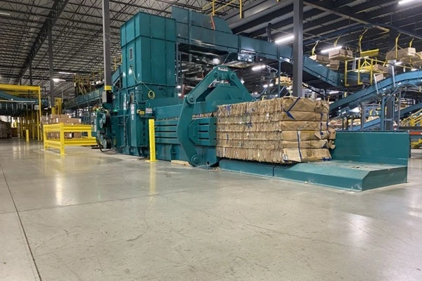 Green industrial baler/shredder in a warehouse with a pallet of bundled material ready for processing
