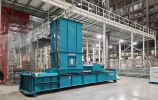 Large blue industrial machine in a spacious factory, with metal catwalks and overhead infrastructure in the background.