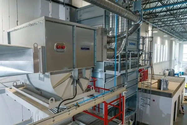 Industrial mechanical room with a large metal air handling unit and connected ducts on a raised platform, showing a red emergency stop button and raised walkways.