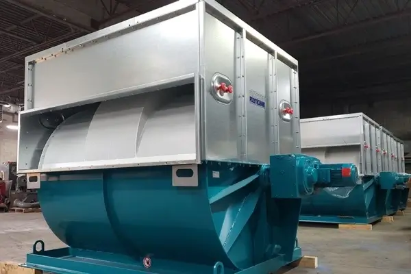 Two large industrial machines with teal lower sections and light gray upper housings on a factory floor, featuring red valve handles and mounted on wooden blocks